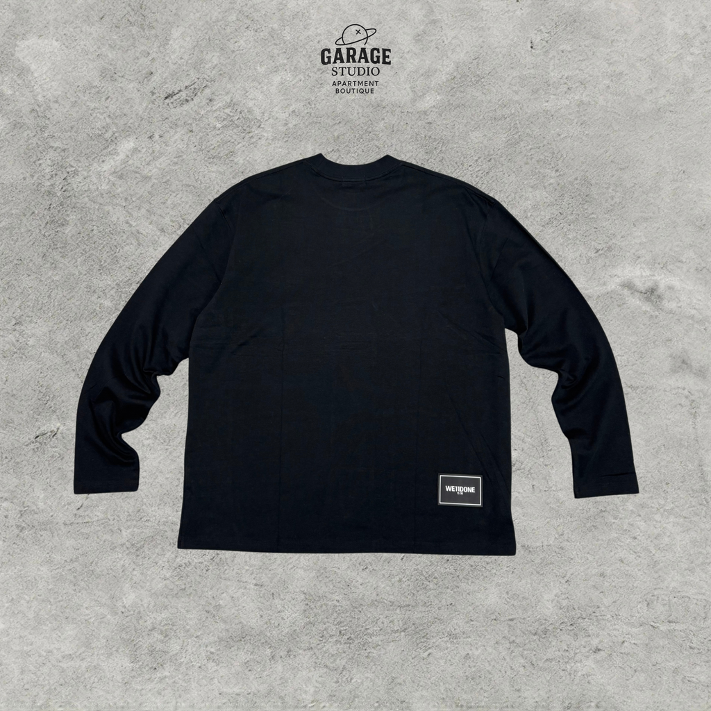 Back of black WE11DONE long-sleeve T-shirt with a small logo patch near the lower hem.
