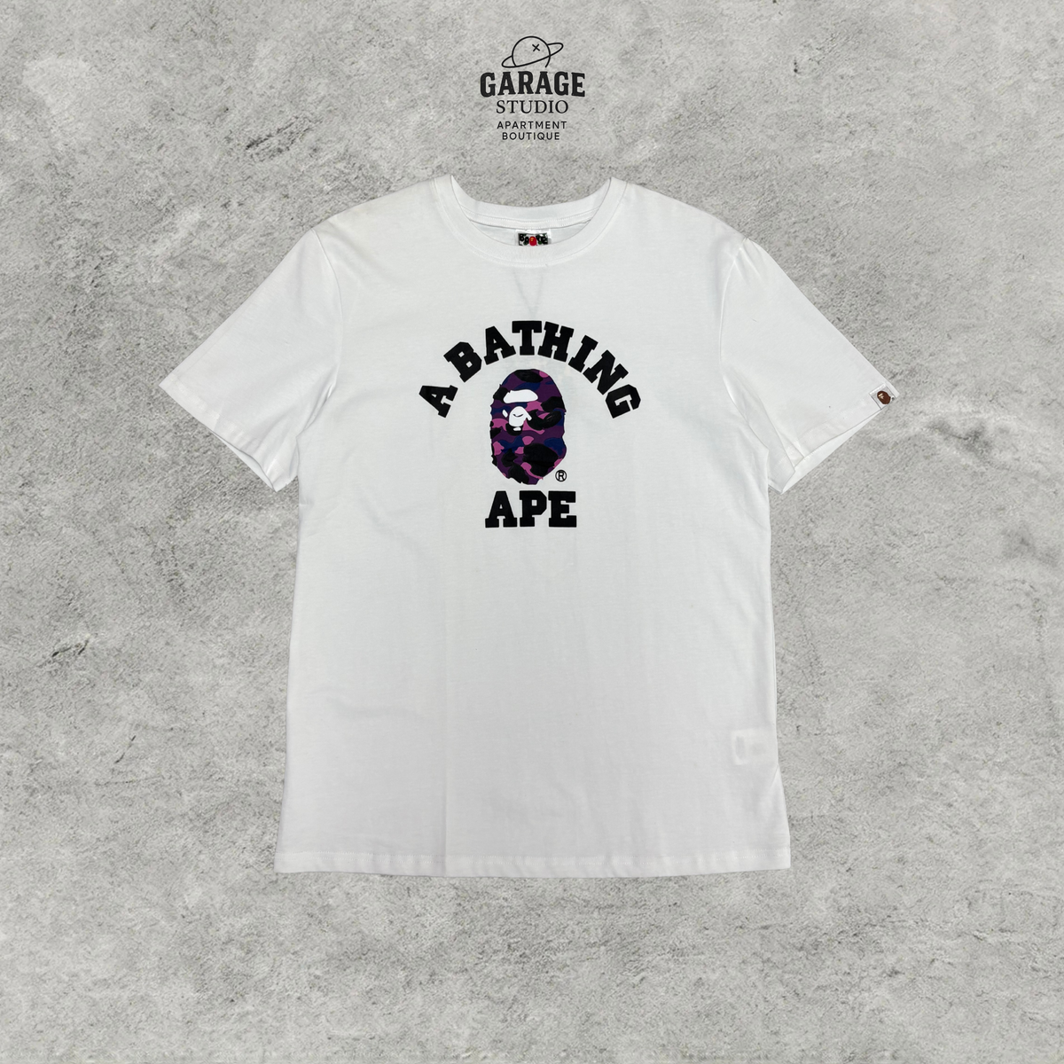 White crew-neck T-shirt with black A BATHING APE lettering and purple camouflage ape-head chest graphic